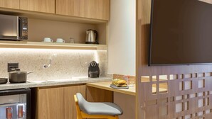A modern kitchen with wooden cabinets, a microwave, a kettle, a coffee maker, and a refrigerator.