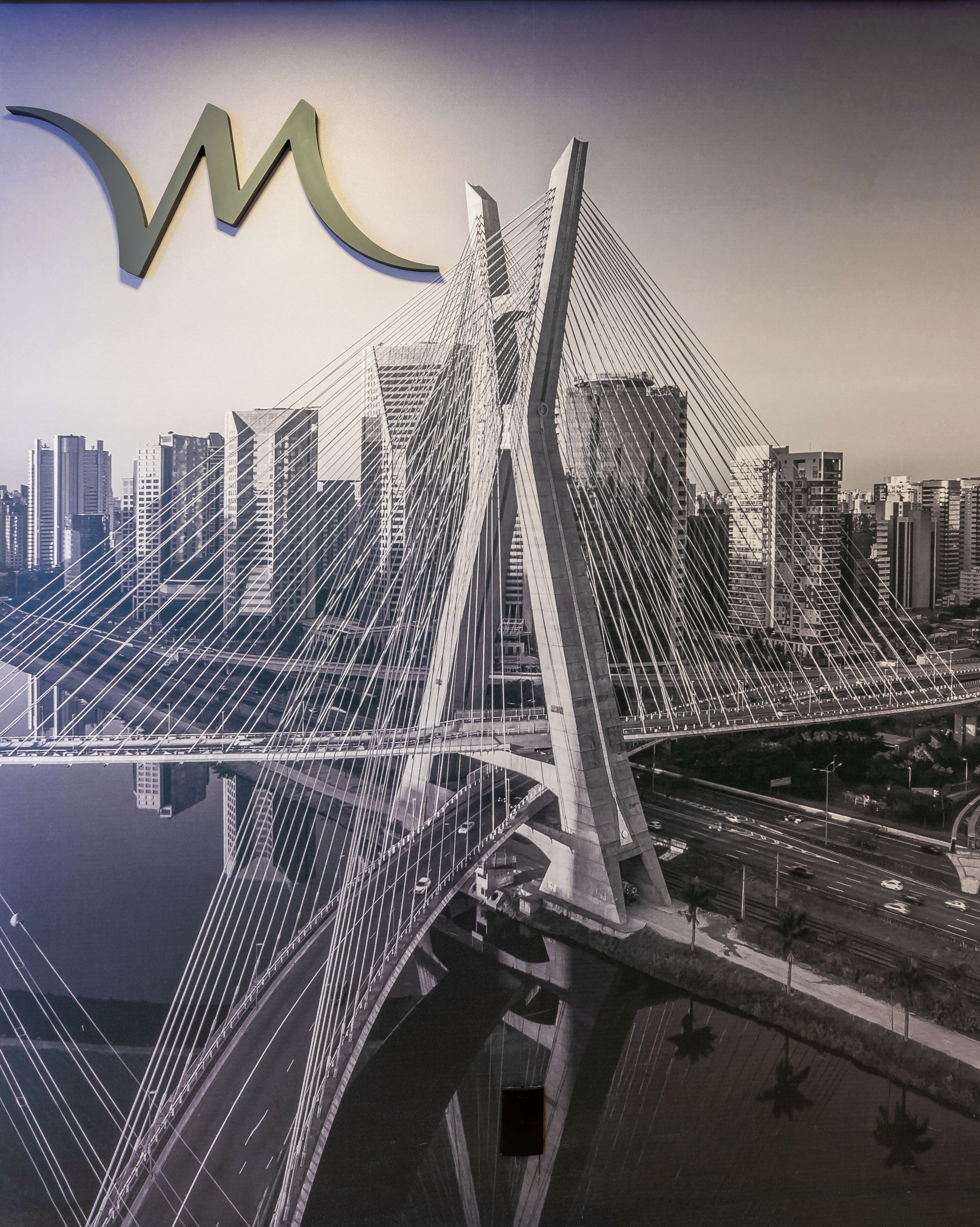 A modern bridge with a complex cable structure, surrounded by high-rise buildings and a body of water.
