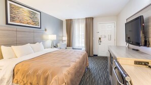 A hotel room with a large bed, a desk with a flat-screen TV, a painting on the wall, and a door. - Quality Inn Gallatin - Nashville Metro (Gallatin)