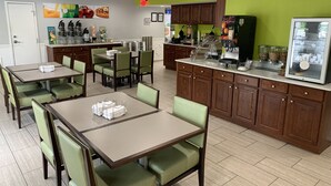 A clean, well-lit cafe with green chairs, wooden tables, and a kitchen area with a coffee machine and food display. - Quality Inn Gallatin - Nashville Metro (Gallatin)