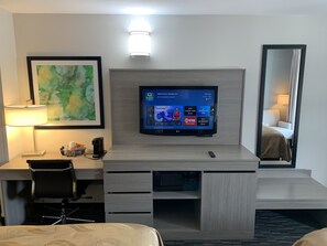 A hotel room with a flat-screen TV mounted on the wall, a desk with a lamp, a chair, and a bed with a headboard. - Quality Inn Gallatin - Nashville Metro (Gallatin)