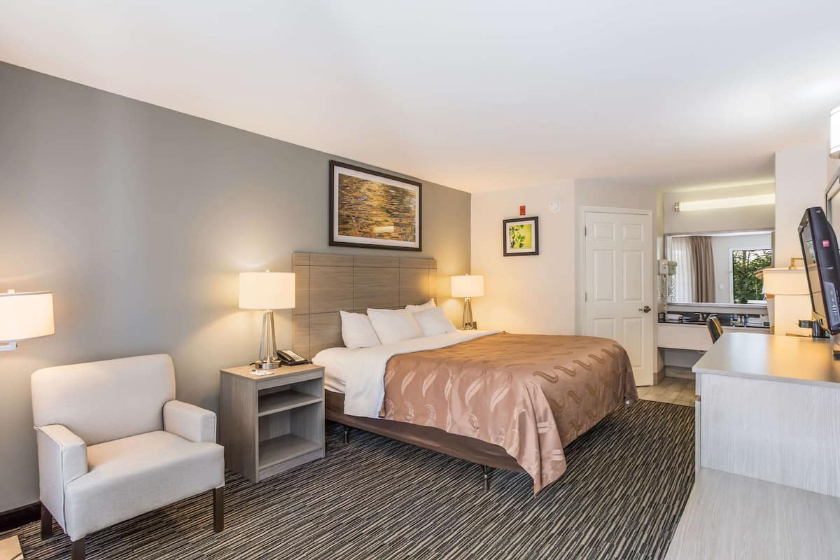 A hotel room with a bed, a chair, a desk, and a door.