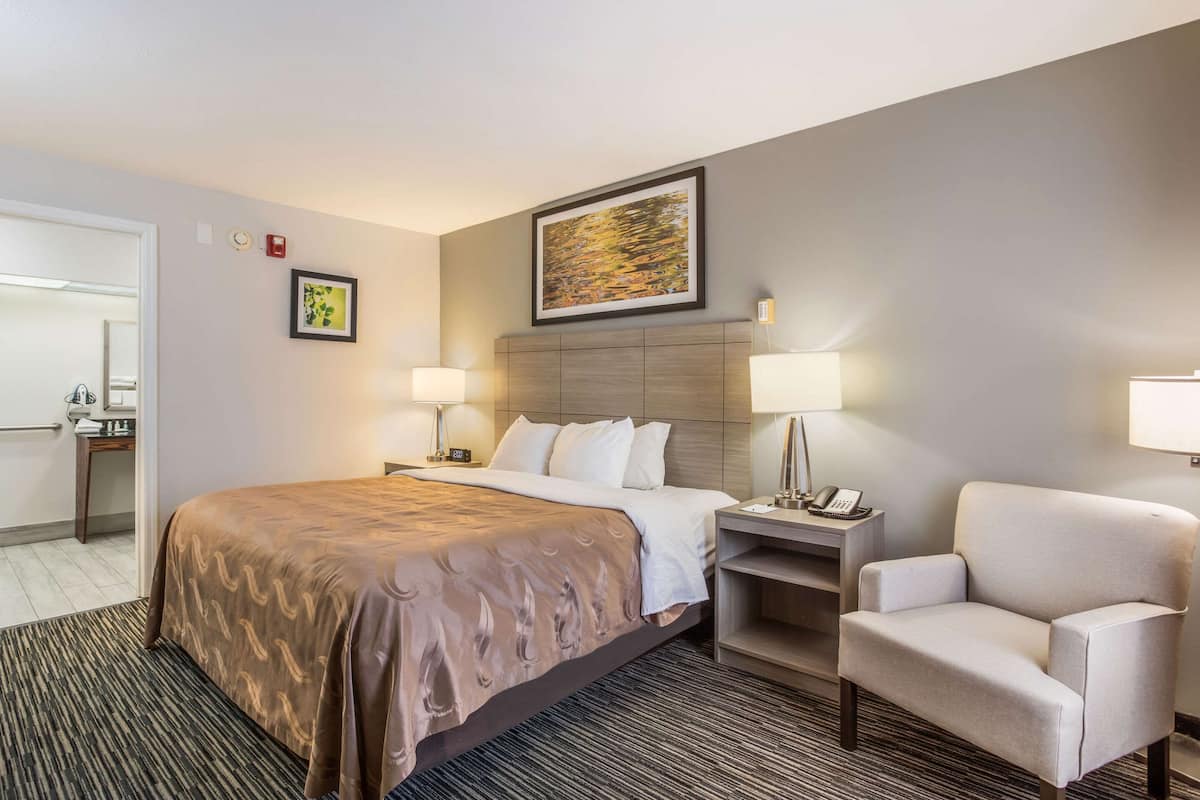 A hotel room with a large bed, two bedside tables with lamps, a chair, a desk, and a framed picture on the wall.