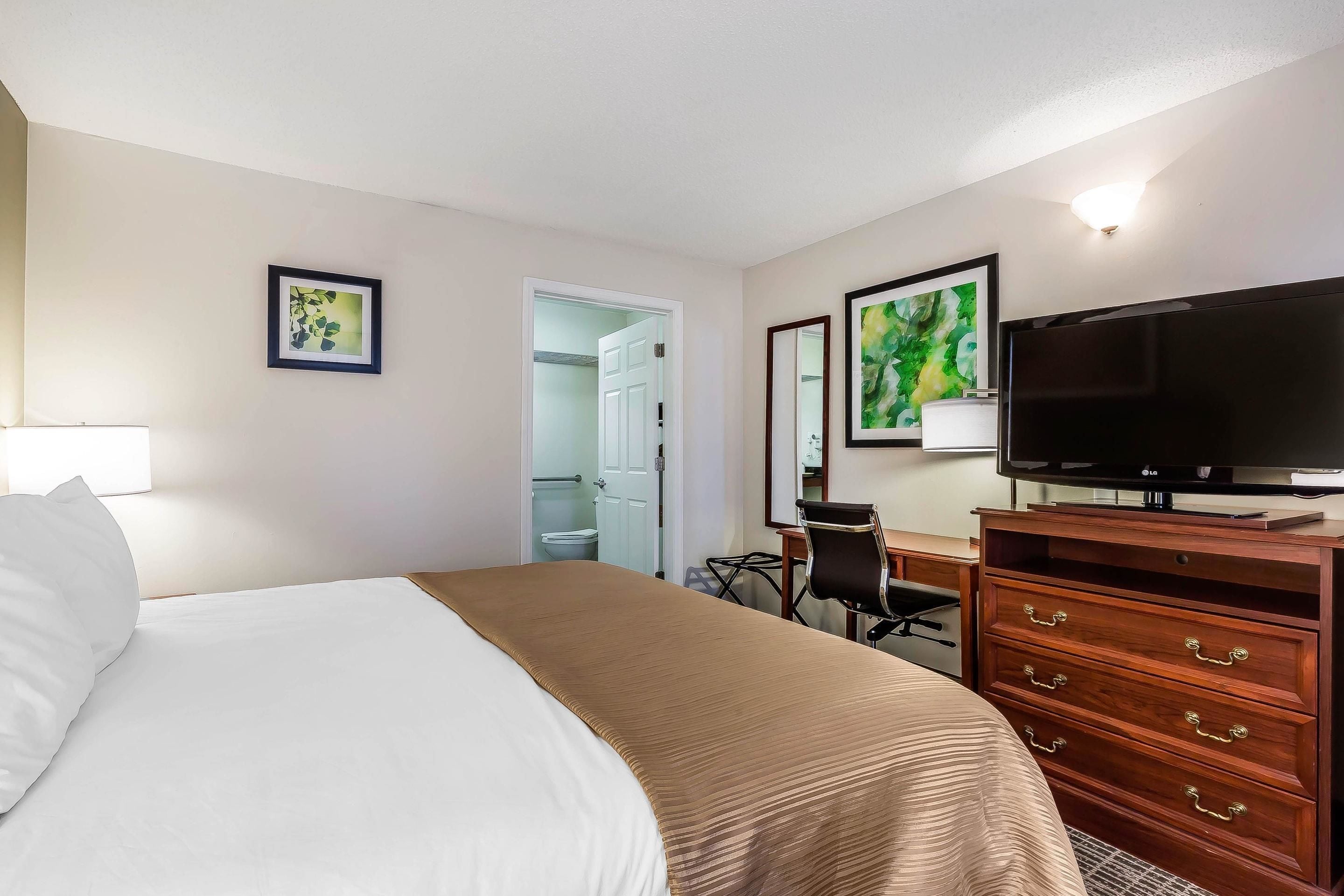 Une chambre d’hôtel avec un lit, une télévision, une commode et un bureau.