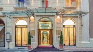 A hotel entrance with a grand archway, a red carpet, and two potted plants. - UNA Hotels Empire Roma (Rome)