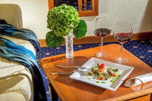 Une table à manger avec une assiette de nourriture, deux verres à vin et un vase rempli de fleurs vertes.
