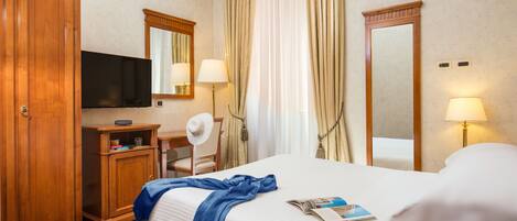 A hotel room with a bed, a television, a desk with a lamp, a mirror, and curtains.