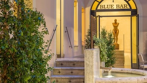 A building entrance with a sign reading "BLUE BAR" and a statue of a woman. There are steps leading up to the entrance, and a small fountain in front. - UNA Hotels Empire Roma (Rome)