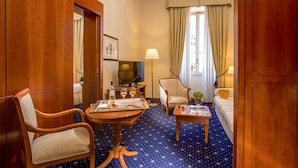 A hotel room with a wooden wardrobe, a television, a sofa, a chair, a table, and a lamp. - UNA Hotels Empire Roma (Rome)