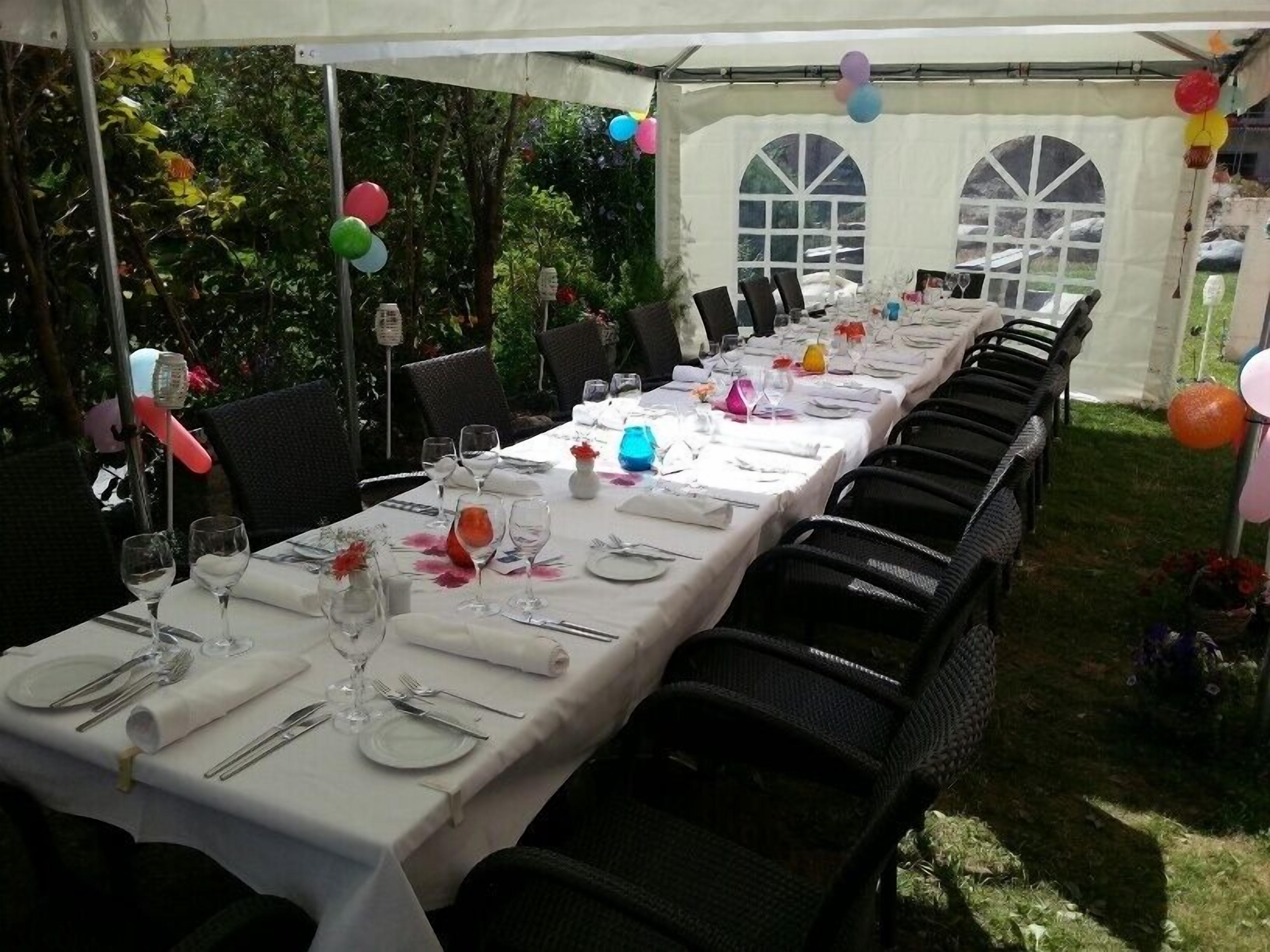 Un área de comedor con carpas, mesas dispuestas para una comida, rodeada de sillas y globos.