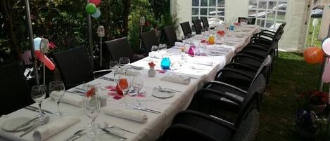 Un área de comedor con carpas, mesas dispuestas para una comida, rodeada de sillas y globos.