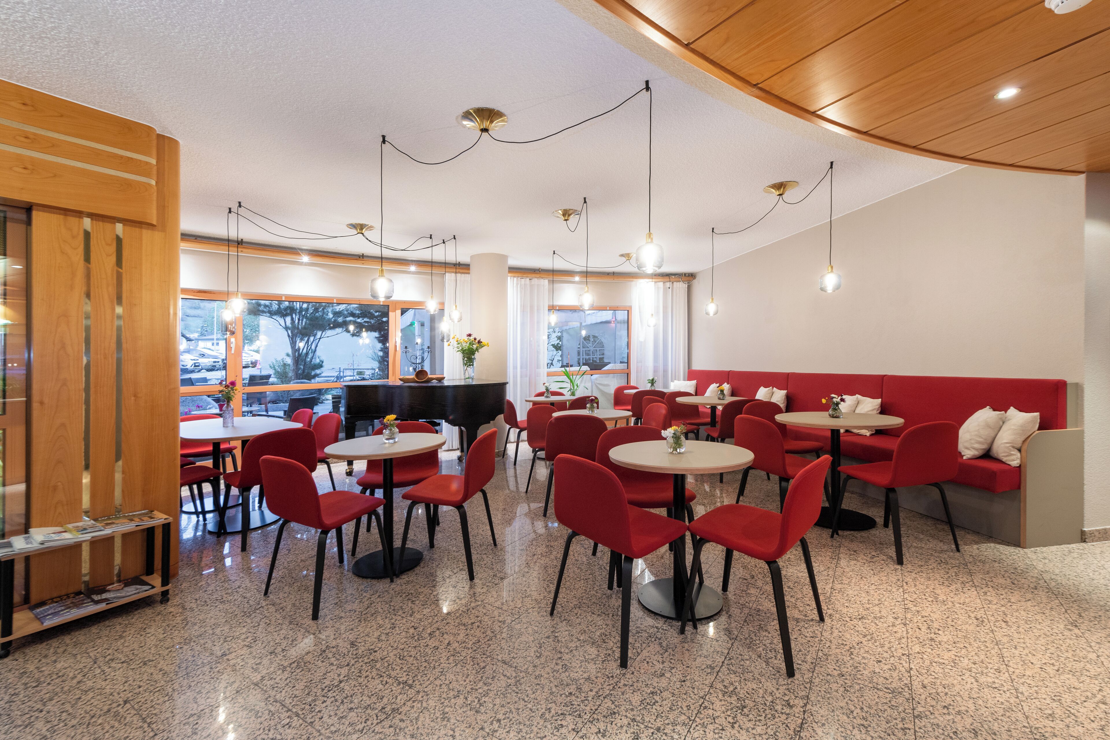Un restaurante moderno con sillas y mesas rojas, detalles de madera y amplios ventanales que ofrecen vistas al exterior.