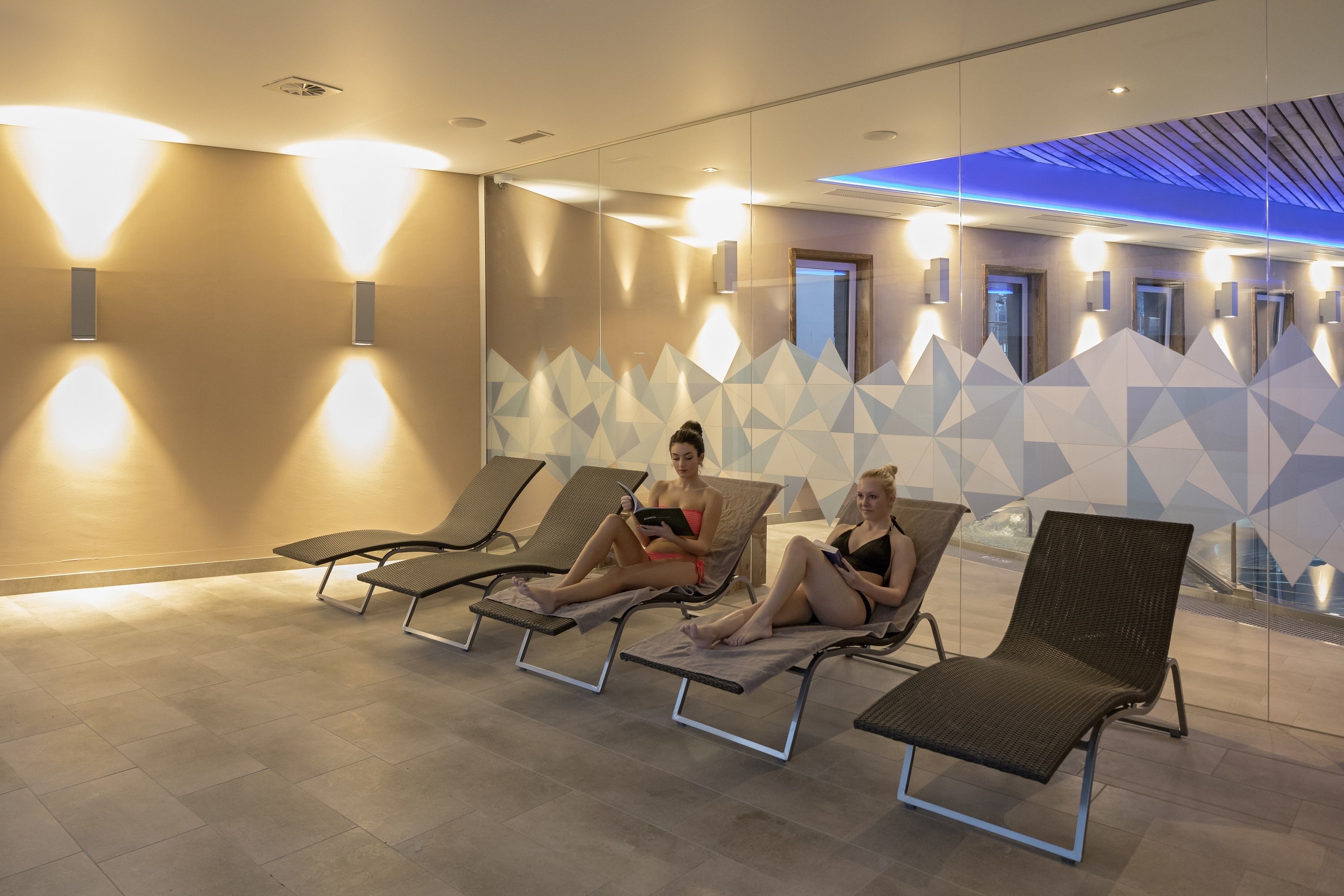 A modern indoor relaxation area with lounge chairs and wall-mounted lights.