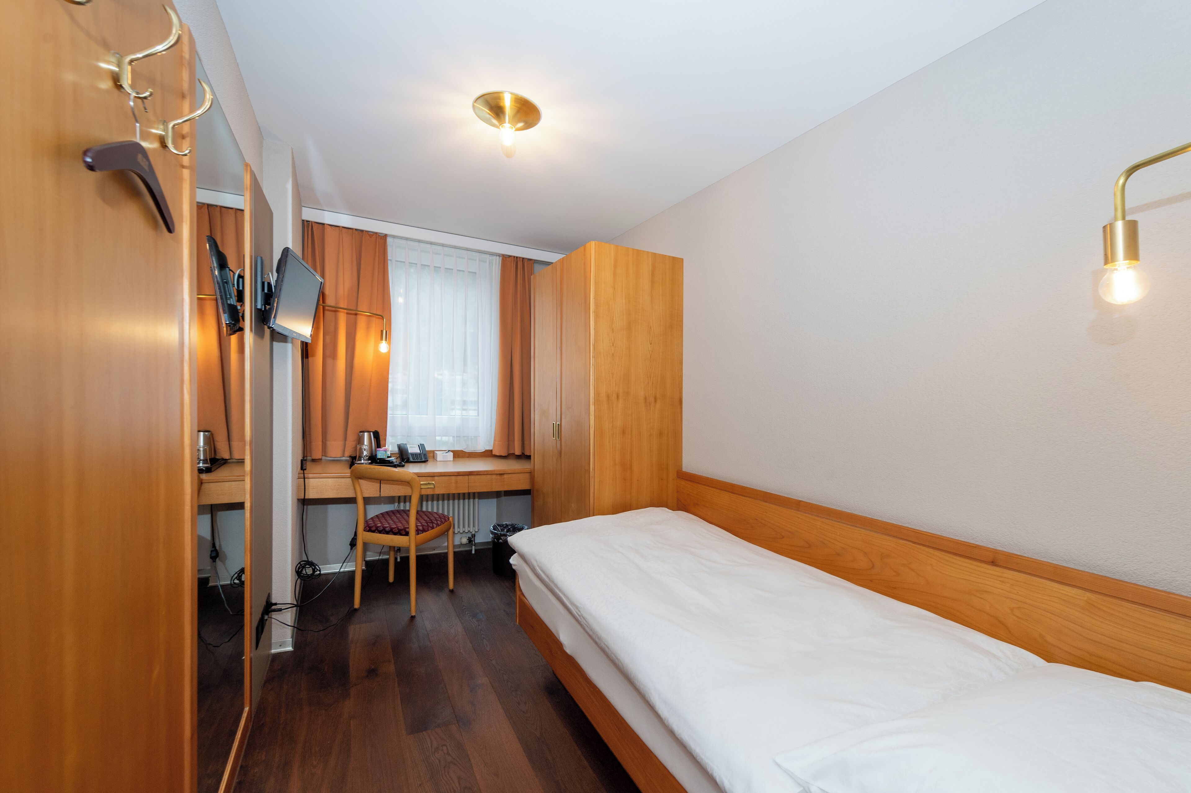 A compact room with a wooden bed, a desk with a chair, and a wardrobe.