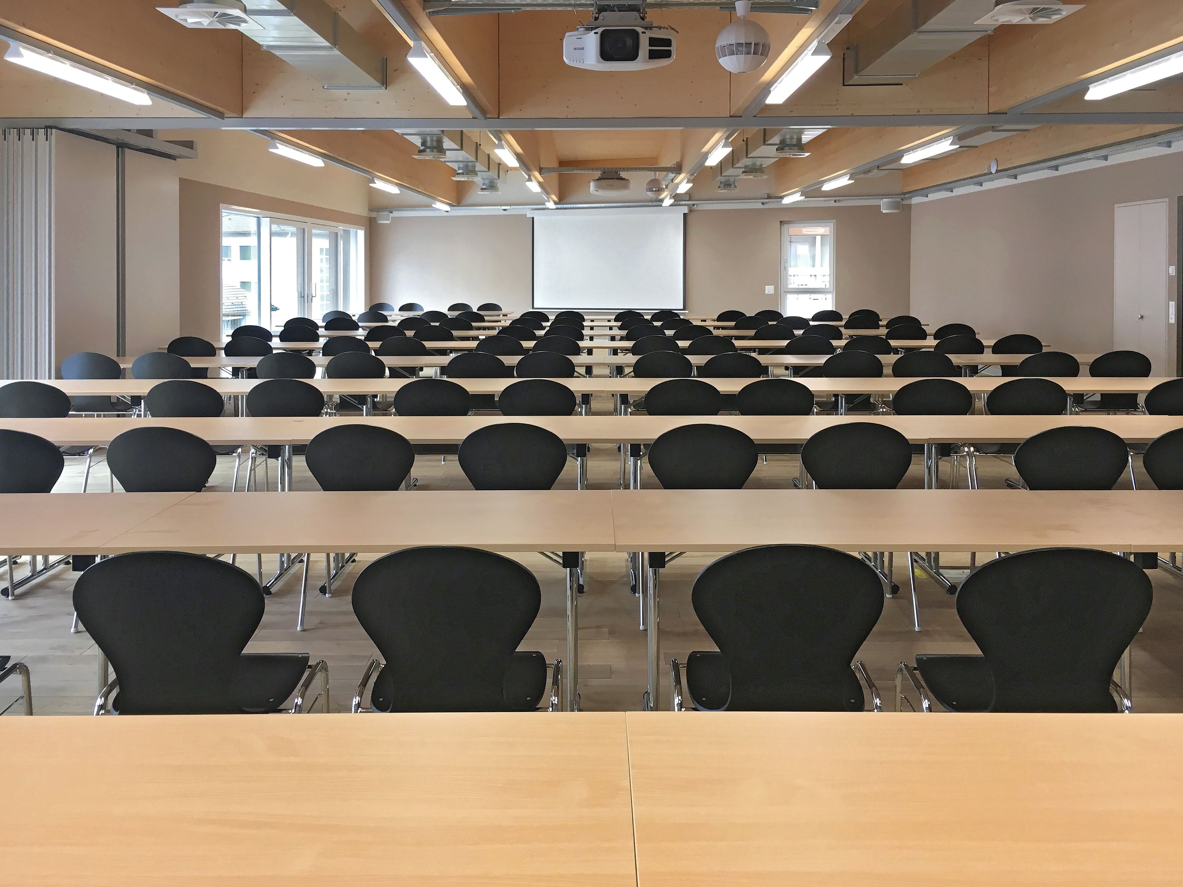 A classroom with rows of desks and chairs, a projector, and a screen.