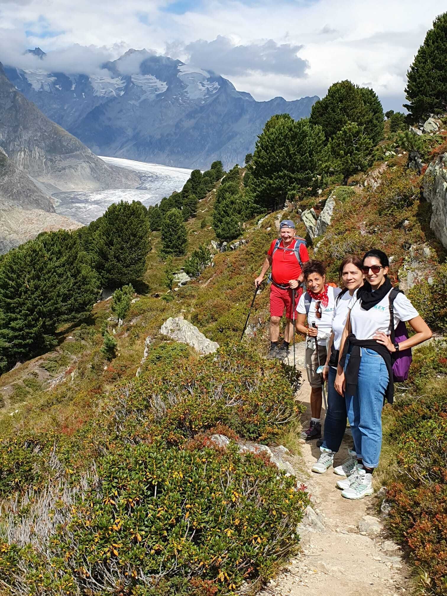 A group of hikers on a mountain trail with a glacier and snow-capped peaks in the background.