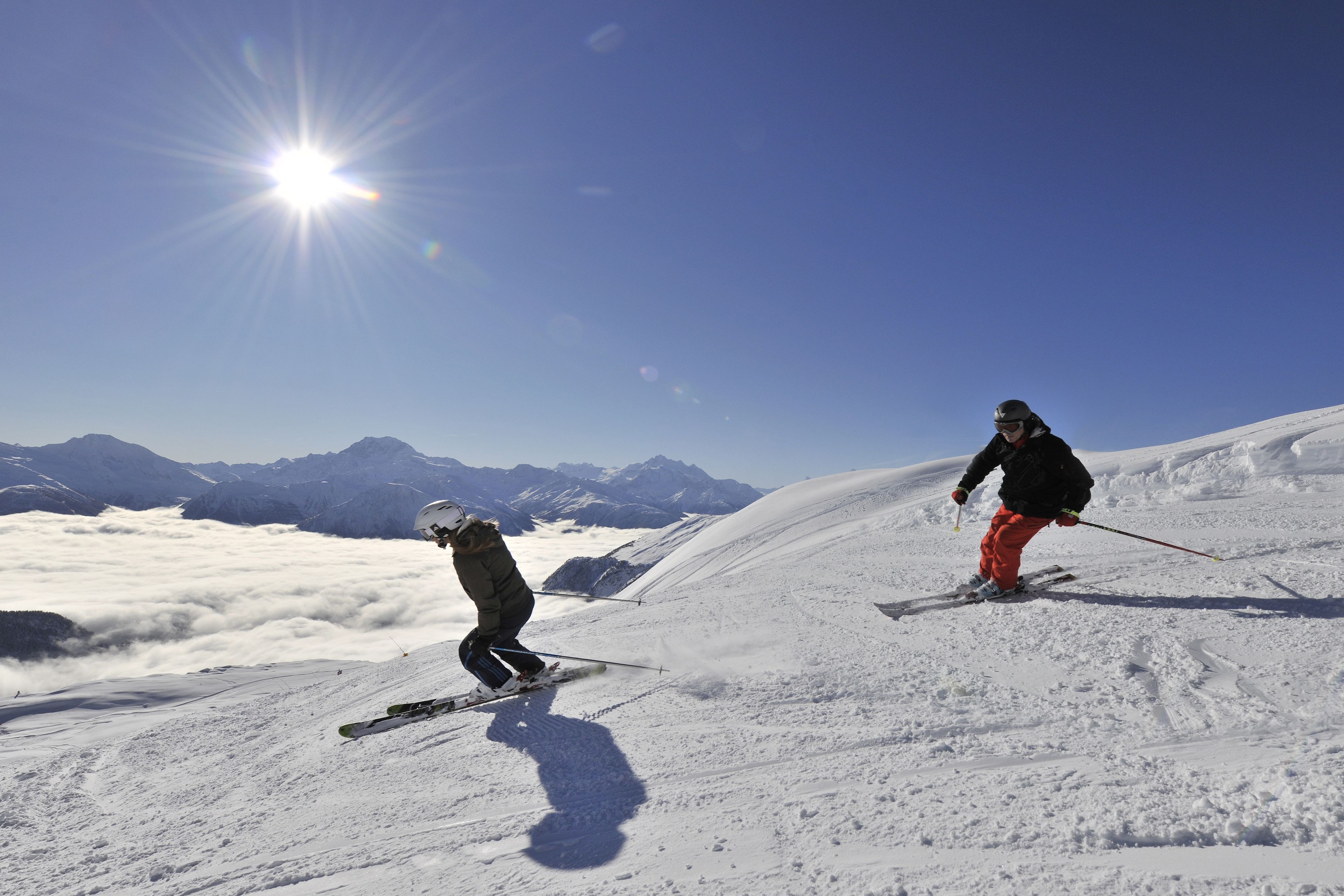 Twee skiërs op een besneeuwde helling, heldere lucht en bergen op de achtergrond.