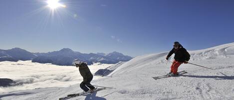 Twee skiërs op een besneeuwde helling, heldere lucht en bergen op de achtergrond.