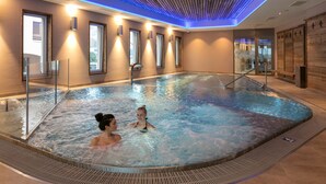 An indoor swimming pool with clear water, wooden ceiling, and modern lighting. - Hotel Alex (Naters)