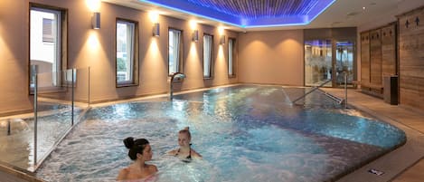 Una piscina interior con agua cristalina, techo de madera e iluminación moderna.