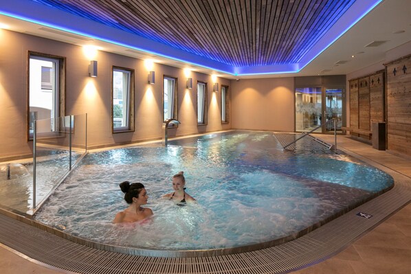 Una piscina interior con agua cristalina, techo de madera e iluminación moderna.