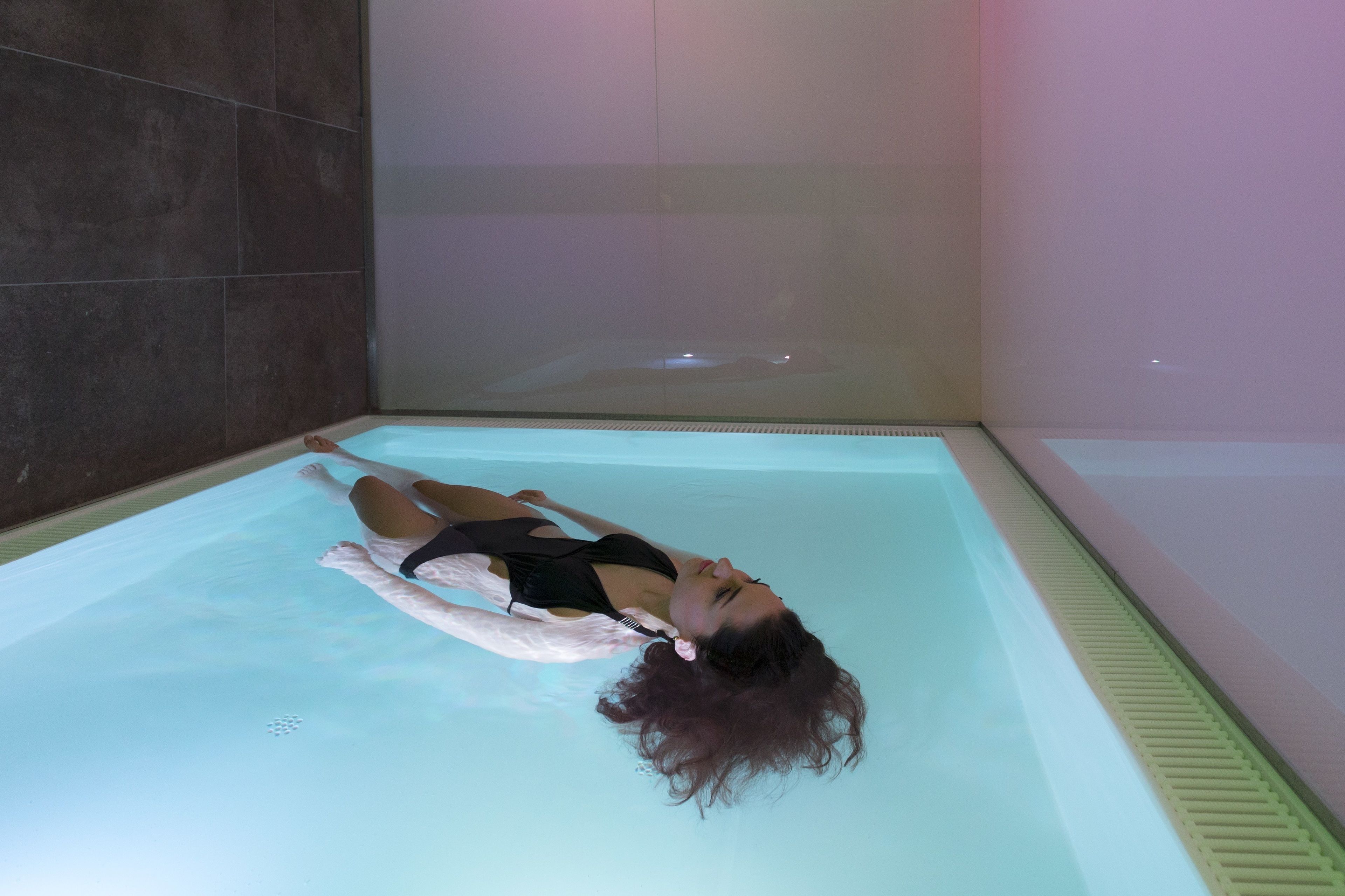 Une personne est allongée dans une piscine rectangulaire à l’eau claire, dont un des murs est recouvert de carreaux et qui est équipée d’un drain sur un côté.