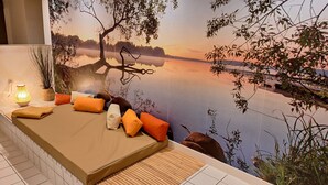 Quarto com cama, almofadas, abajur e um mural de um lago ao pôr do sol.