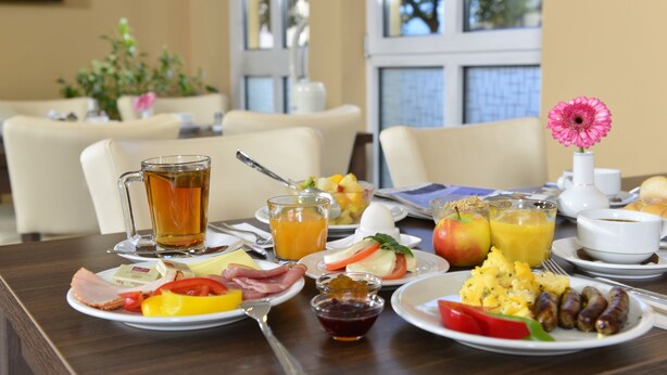 Mesa de café da manhã com pratos de comida, um copo de suco de laranja, um copo de chá e uma flor.