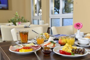 Una mesa de desayuno con platos de comida, un vaso de jugo de naranja, un vaso de té y una flor.