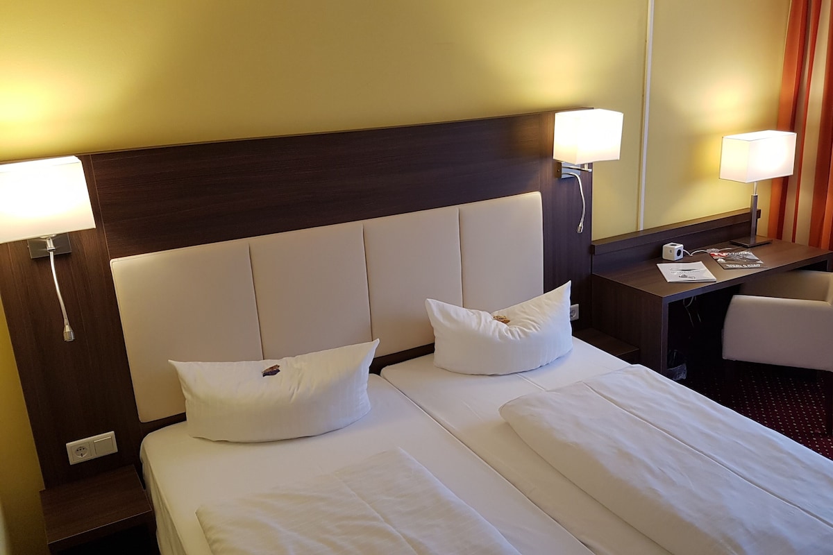 A hotel room with two beds, a desk, a chair, and a window with curtains.
