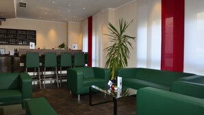 Uma área de recepção com assentos verdes, um balcão de recepção e um bar ao fundo.