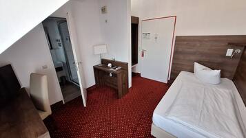 Una habitación de hotel con una cama, un escritorio con una lámpara, un espejo y una puerta que da a un baño.