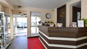 Uma área de recepção com balcão de madeira, um relógio e um tapete vermelho que leva à entrada.