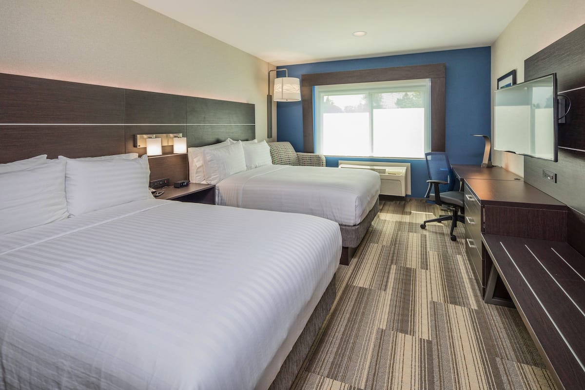 Une chambre d’hôtel avec deux lits, un bureau, une chaise, une télévision et une fenêtre.