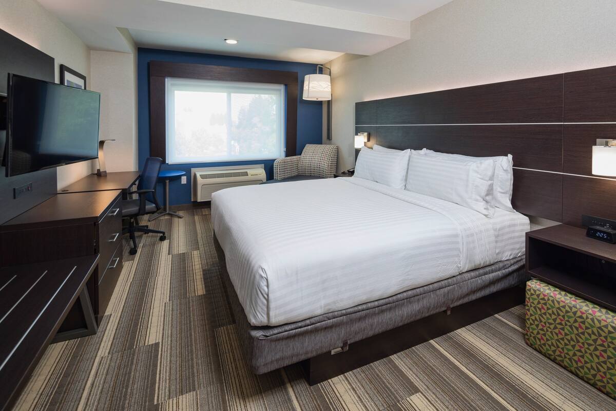 Une chambre d’hôtel avec un grand lit, un bureau doté d’un téléviseur à écran plat, une chaise, une petite table et une fenêtre donnant sur un paysage agréable.