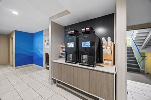 Een koffiehoek met twee koffieautomaten en een toonbank met koffie-dispenser.