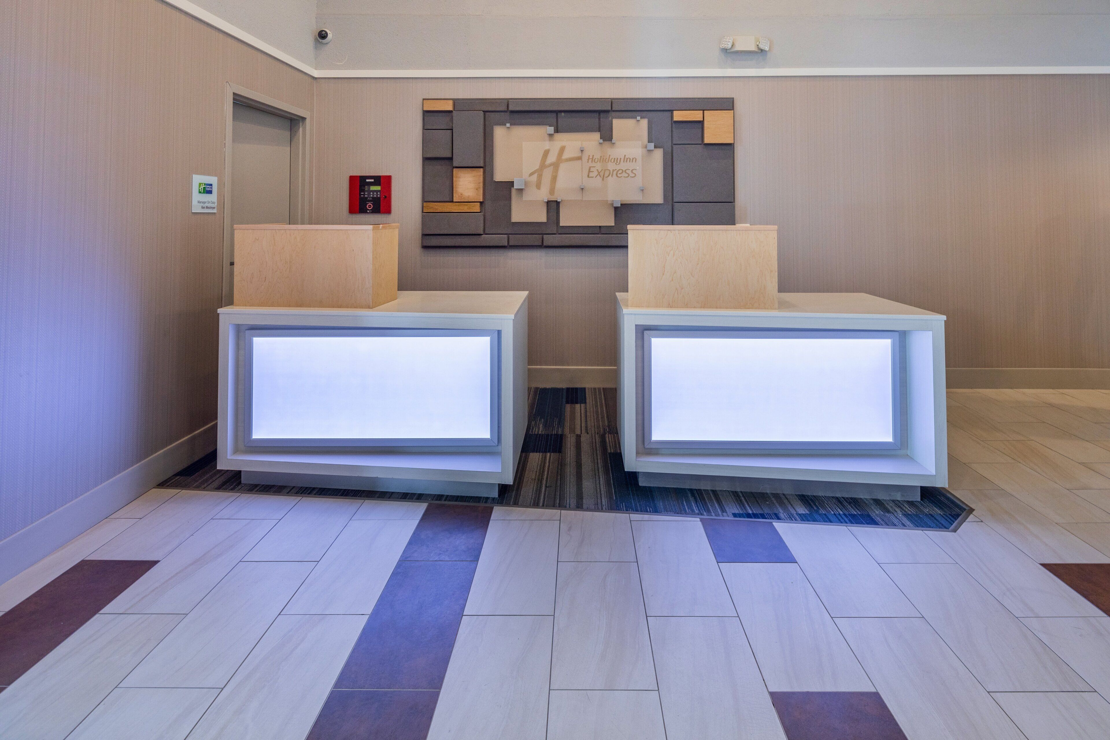 A reception area with two reception desks, a wall-mounted information board, and a security intercom system.