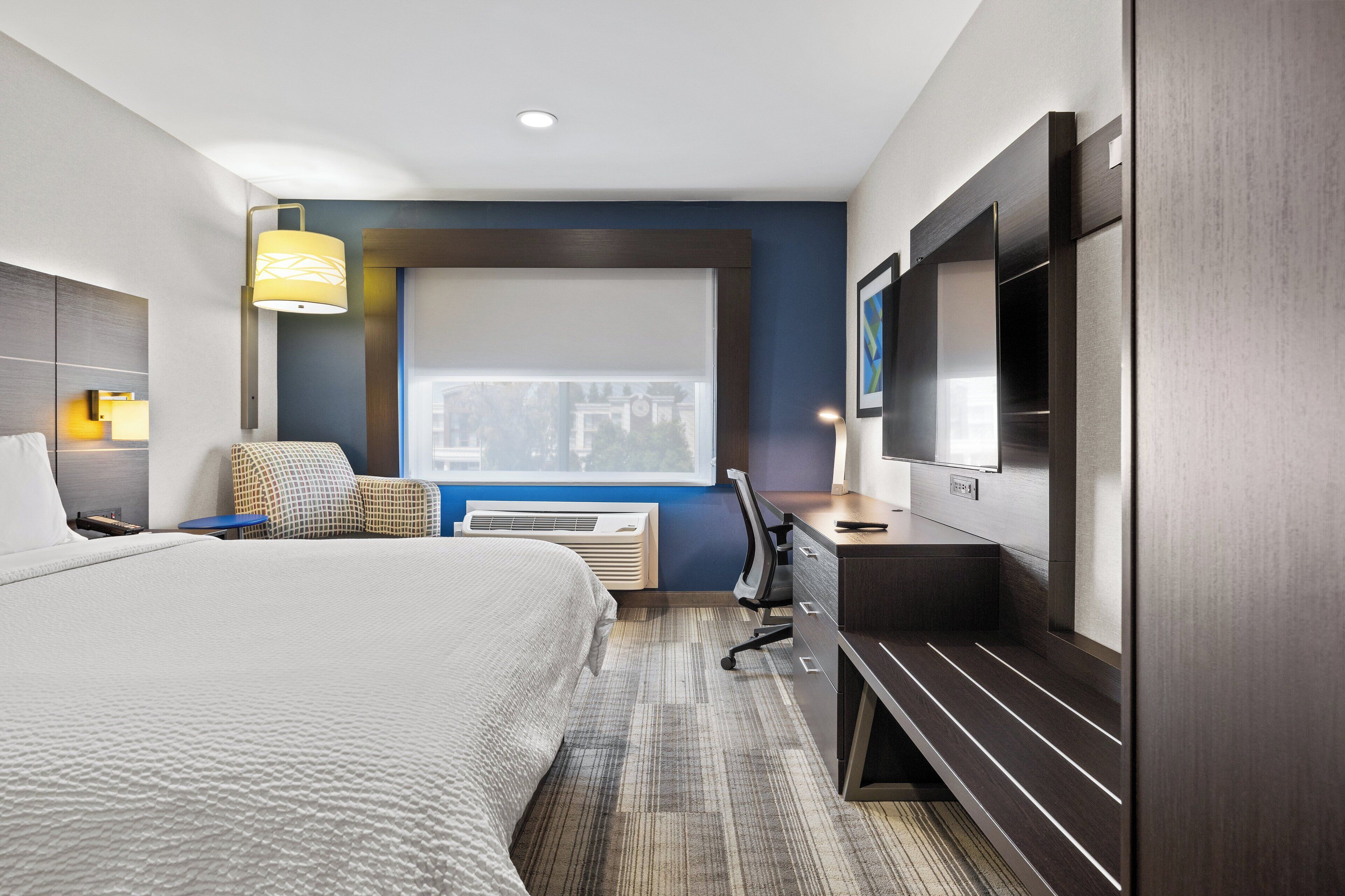 Habitación de hotel con cama, escritorio, silla, televisor y ventana.