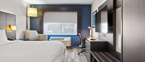 Habitación de hotel con cama, escritorio, silla, televisor y ventana.
