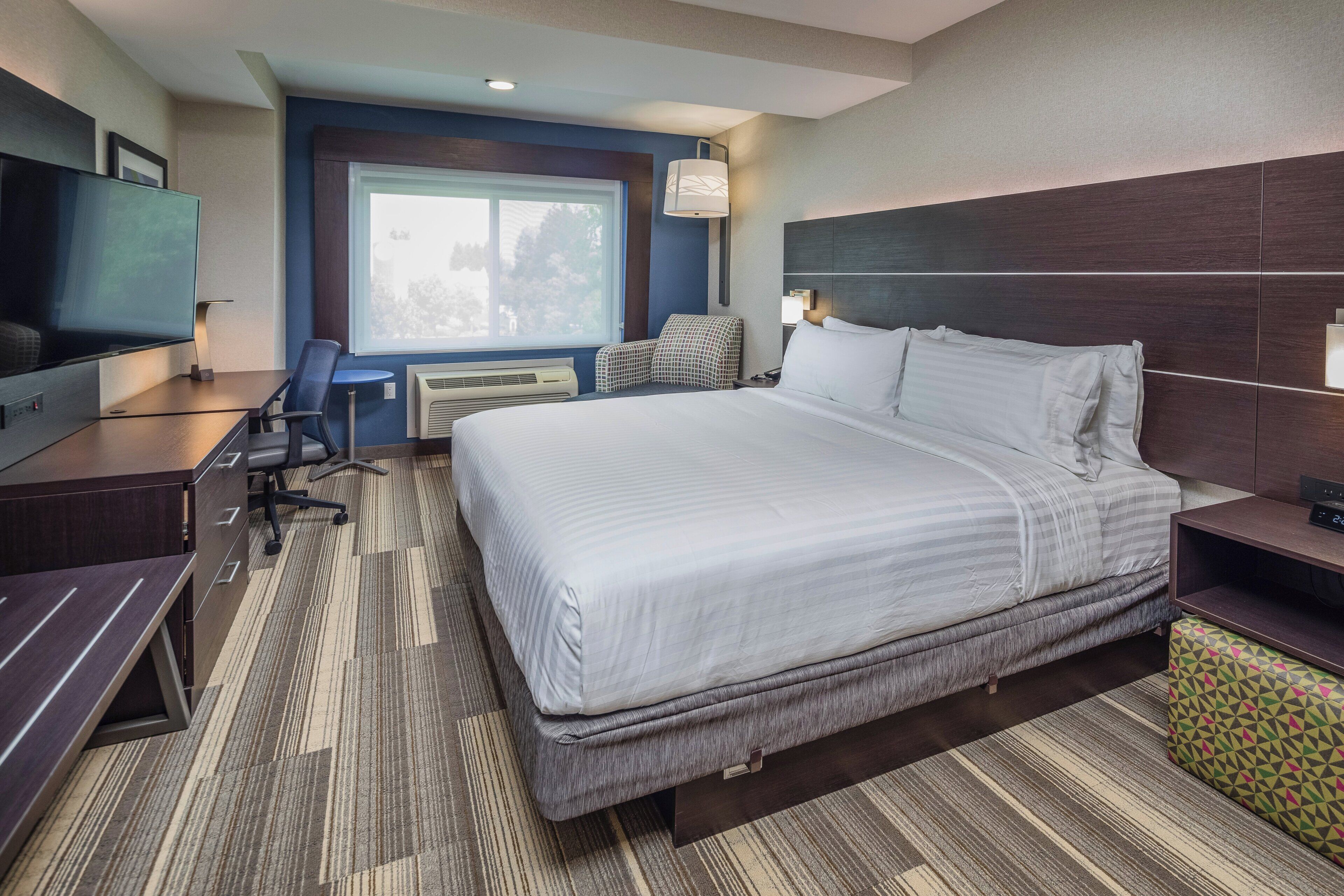 A hotel room with a large bed, a desk with a chair, a television, and a window with a view.