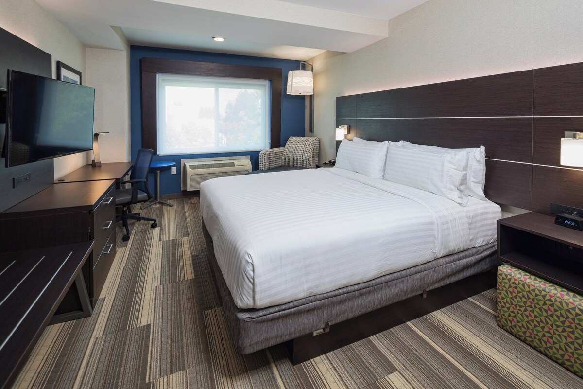 Een hotelkamer met een groot bed, een bureau met een flatscreen televisie, een stoel, een bureaulamp en een raam met uitzicht.