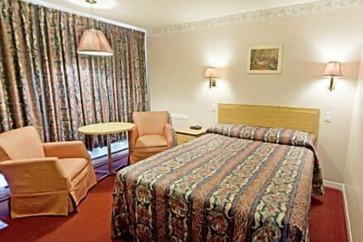 Una habitación de hotel con una cama, dos sillones, una mesita y una lámpara.