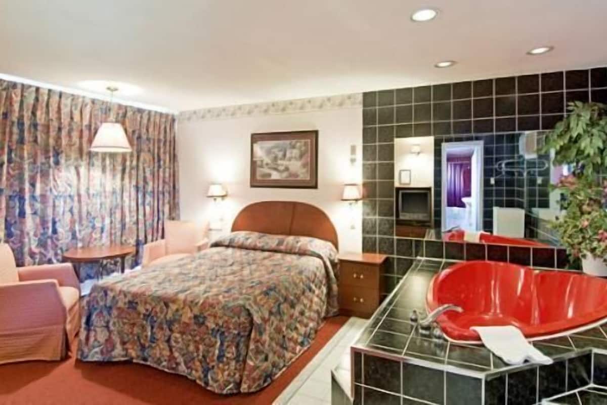 Habitación de hotel con cama, una bañera roja, una silla y un escritorio.