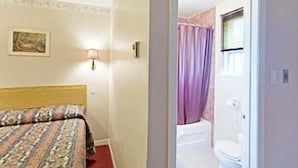 Habitación de hotel con cama, lámpara, un cuadro en la pared y vista al baño por una puerta abierta.
