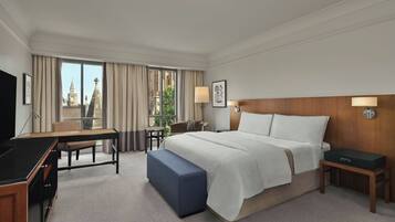Ein Hotelzimmer mit einem Bett, einem Schreibtisch, einem Sessel, einem Fernseher und Blick auf ein Gebäude durch das Fenster.
