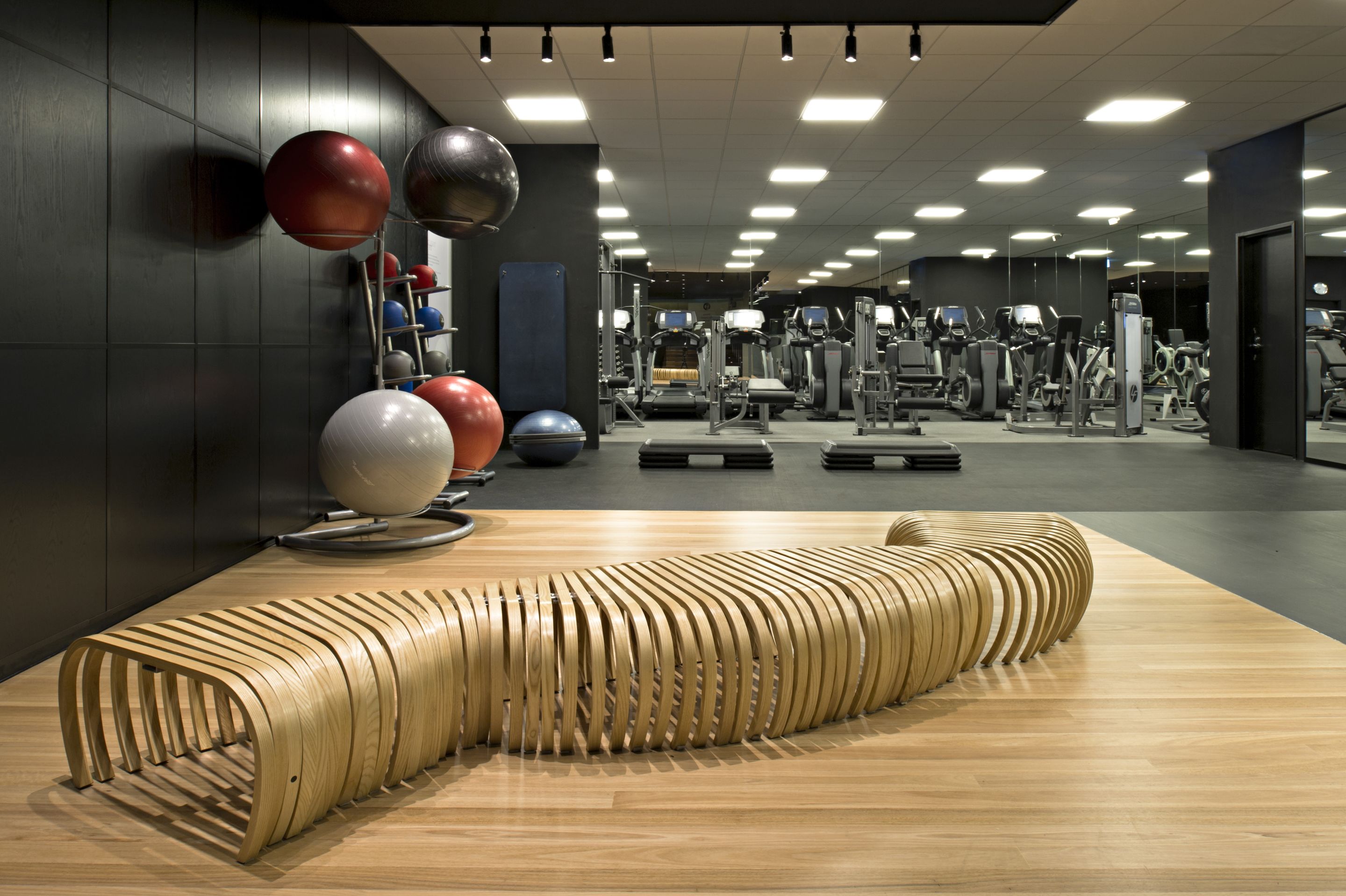 A gym with exercise equipment, a wooden bench, and a wall with exercise balls.