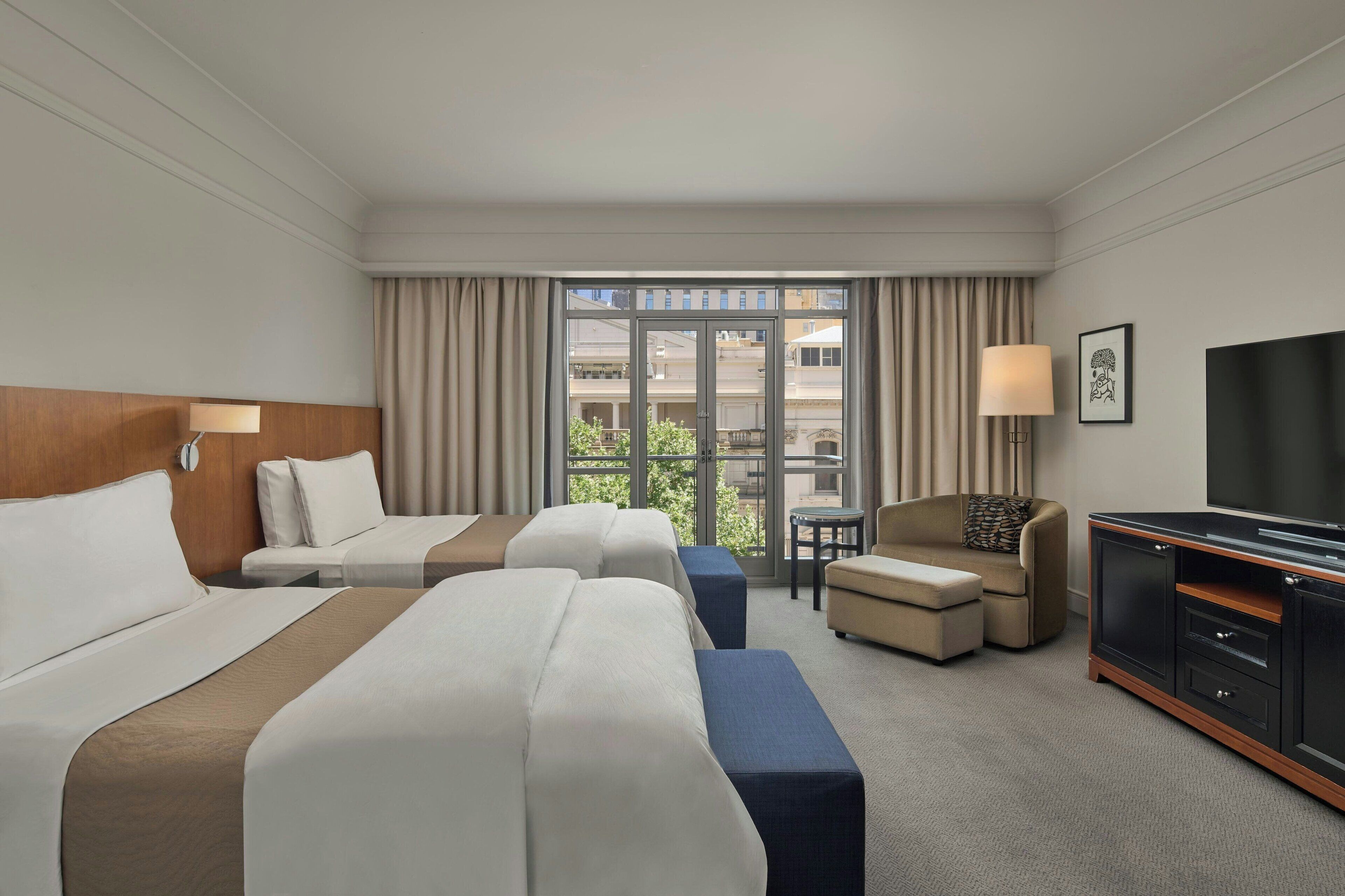 A hotel room with two beds, a sofa, a TV, and a window with curtains.