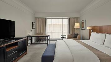 A hotel room with a large bed, a TV, a desk, and a window with curtains.
