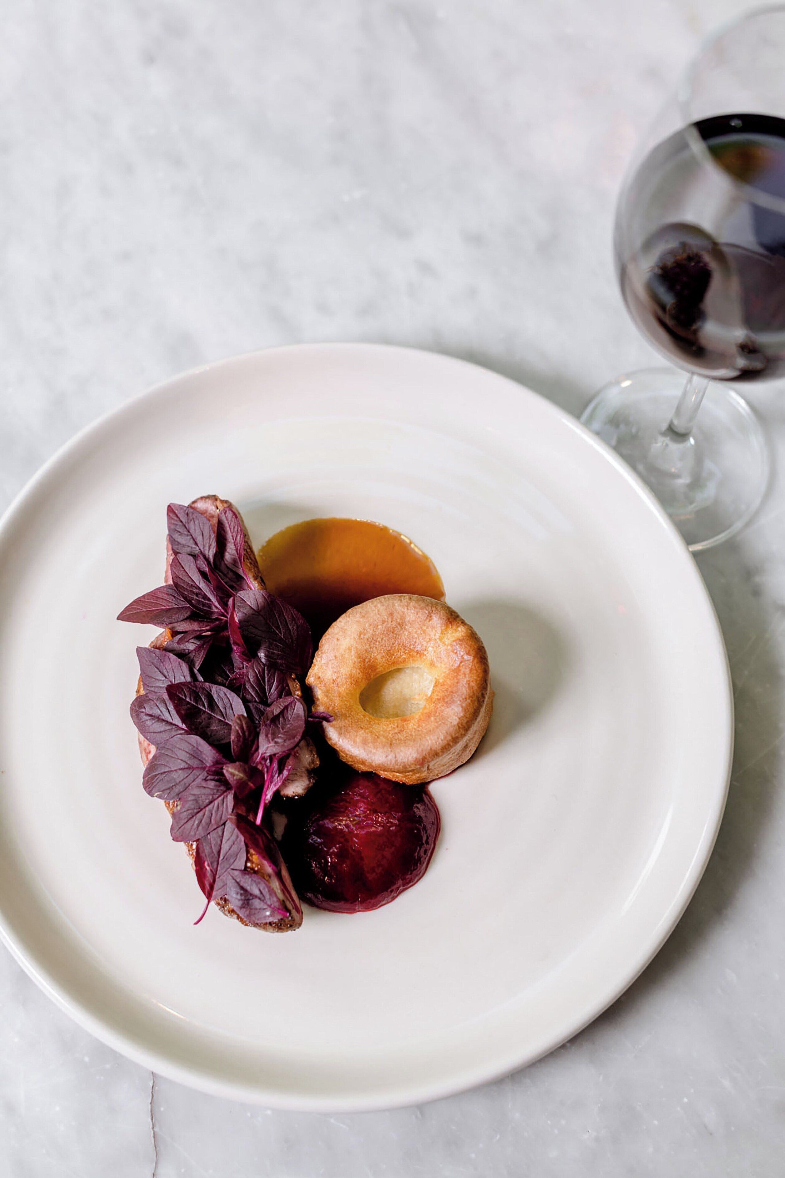 Um prato branco com sobremesa, um copo de vinho tinto e uma toalha de mesa branca.