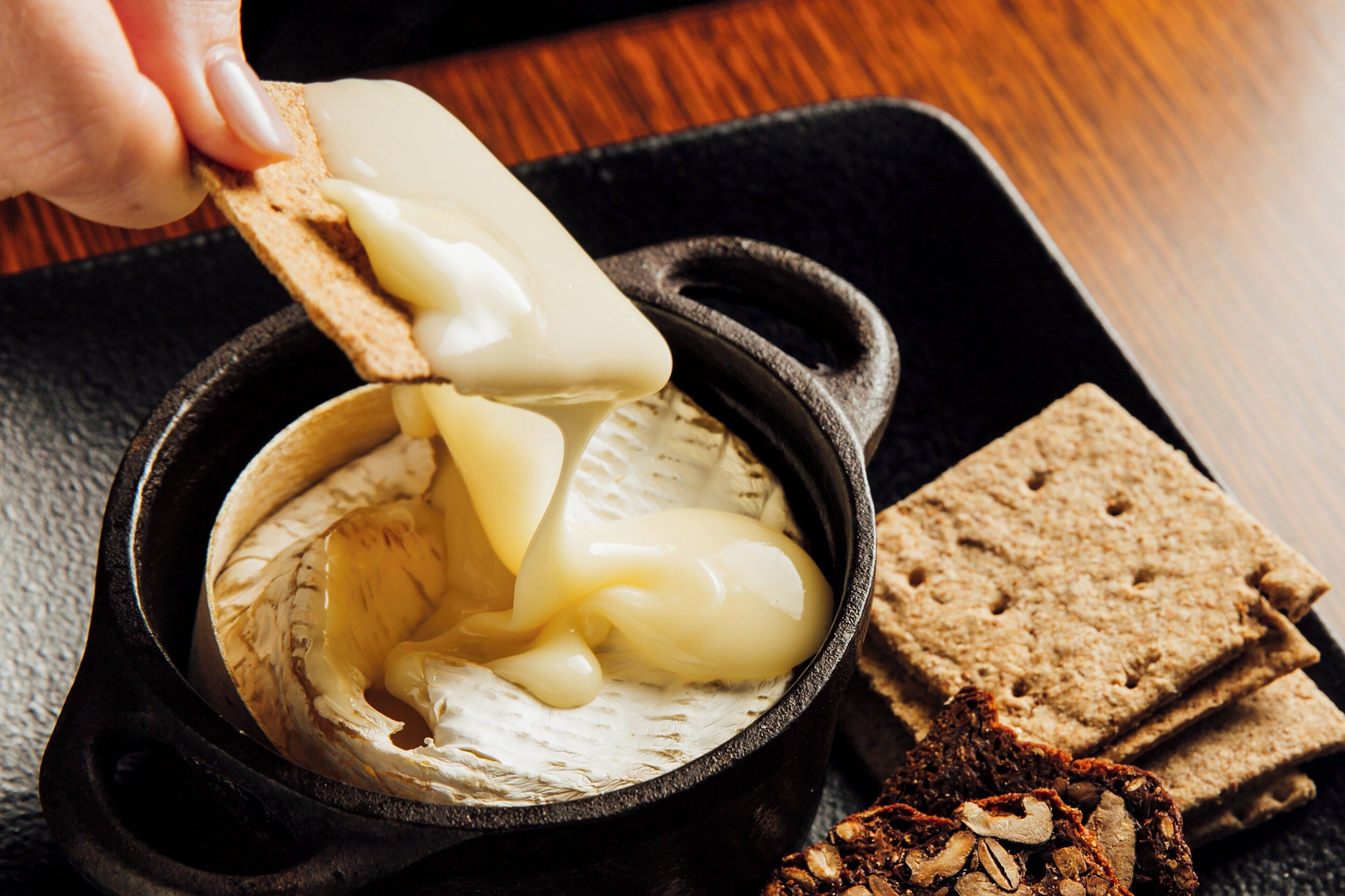 Una tabla de queso de hierro fundido negro con queso derretido y galletas.